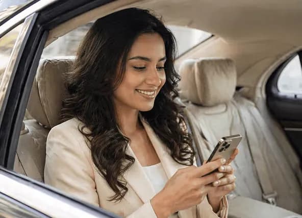 A woman in a car smiles while looking at her smartphone.