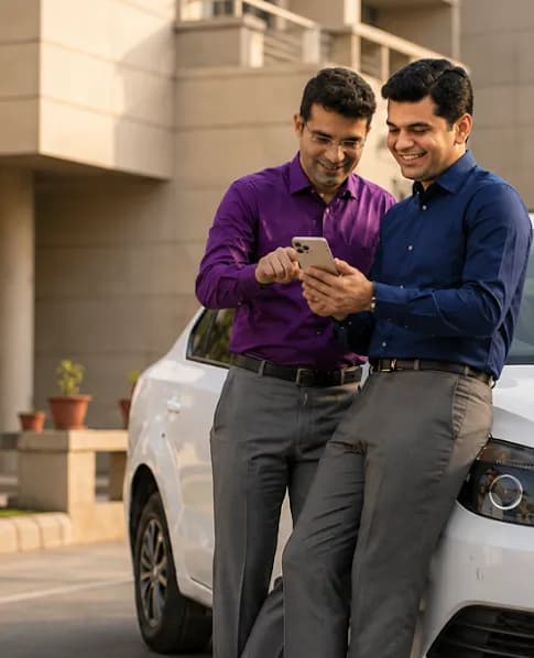 Two smiling men in dress shirts look at a smartphone while leaning on a white car.