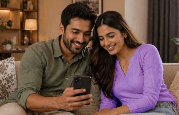 Happy couple sitting on couch, smiling, looking at a smartphone together.